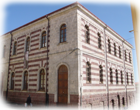Villanova Monteleone e il Palatu 'e sas Iscolas fu realizzato tra il 1890 e il 1920 su progetto dell'ingegnere Achille Dettori. La singolare costruzione ha forme solide e compatte e, sfruttando il dislivello del terreno, passa da due a tre piani, sottolineando il basamento con un alto zoccolo di trachite rossa. Fasce bicrome rosse e grigie caratterizzano fortemente l'edificio, ricorrendo ad un linguaggio neomedioevale, che richiama la bicromia dell'architettura romanica in Sardegna. Le finestre si sviluppano regolarmente e simmetricamente ed hanno tutte forma ad arco come i portali d'ingresso. Datazione soggetto: 1890-1920.